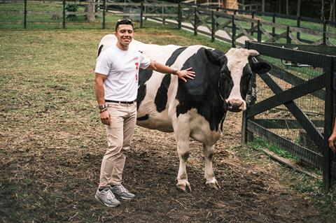 Shawn Rashid stood with his hand on a large cow while wearing a white branded T-Shirt with SR32 in red letter on the front